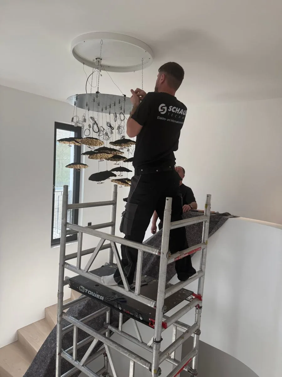 Zwei Monteure montieren eine große Designleuchte im Treppenhaus